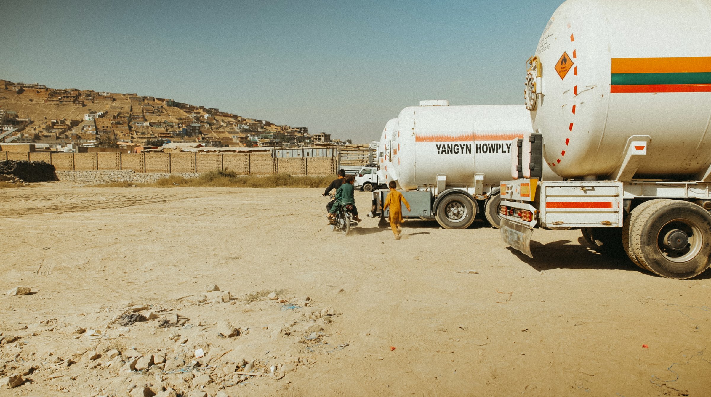 Une route poussiéreuse avec des camions-citerne et des collines en arrière-plan.
