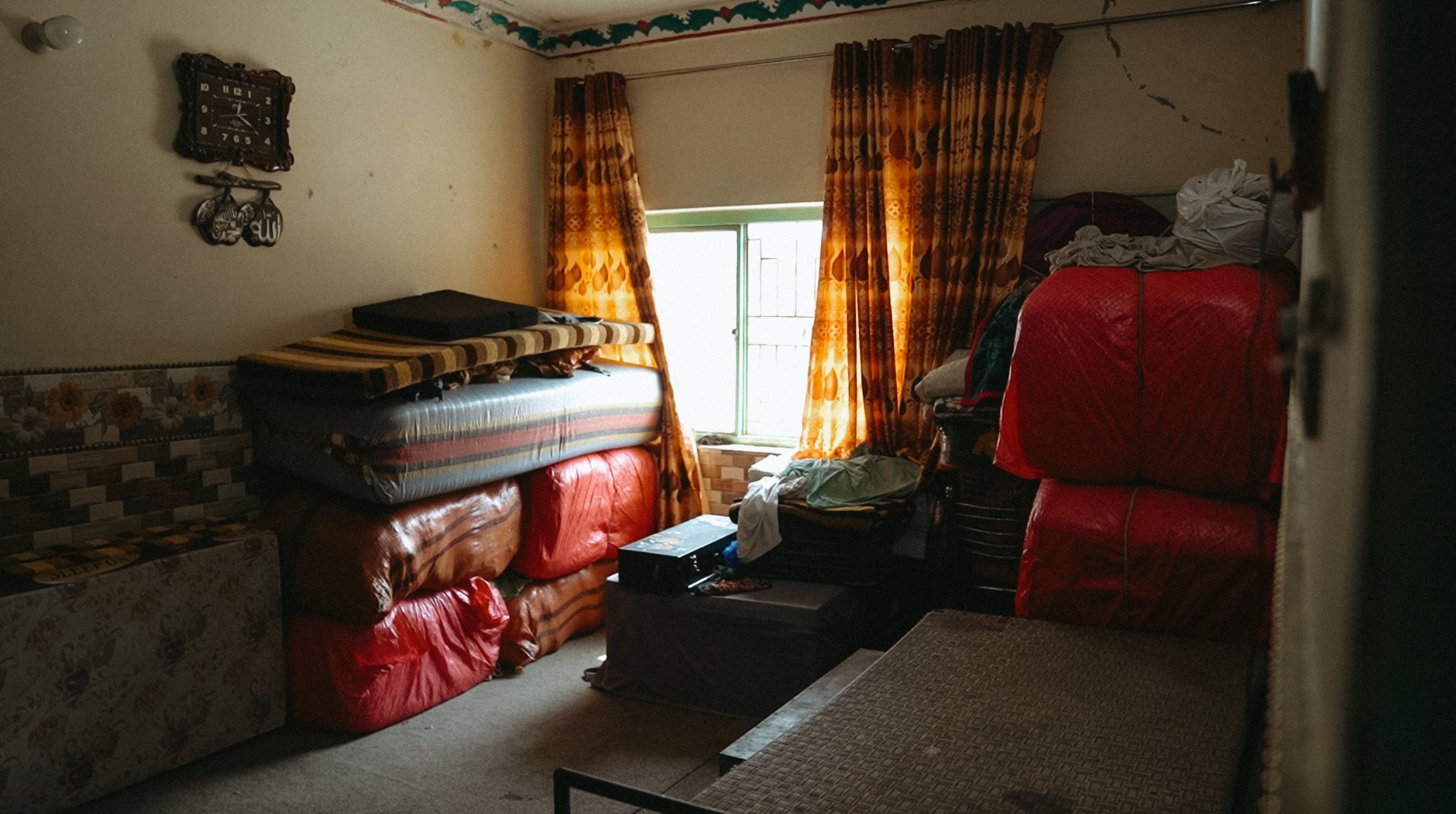 Chambre encombrée avec des matelas empilés et des rideaux à motifs.