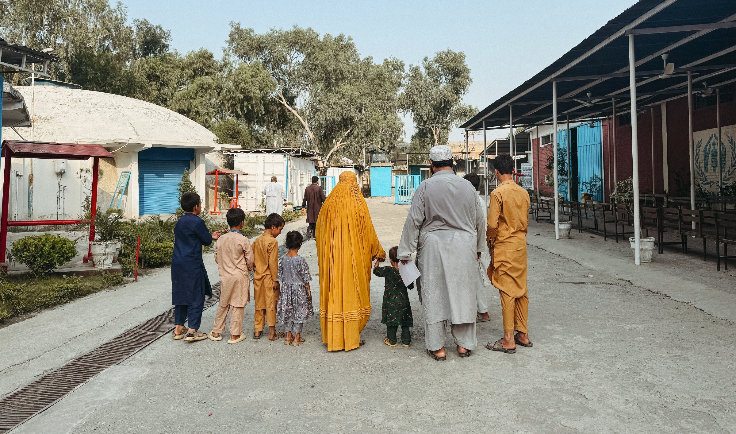 Un groupe d'enfants et d'adultes, tous vêtus de couleurs variées, marchent dans une cour.