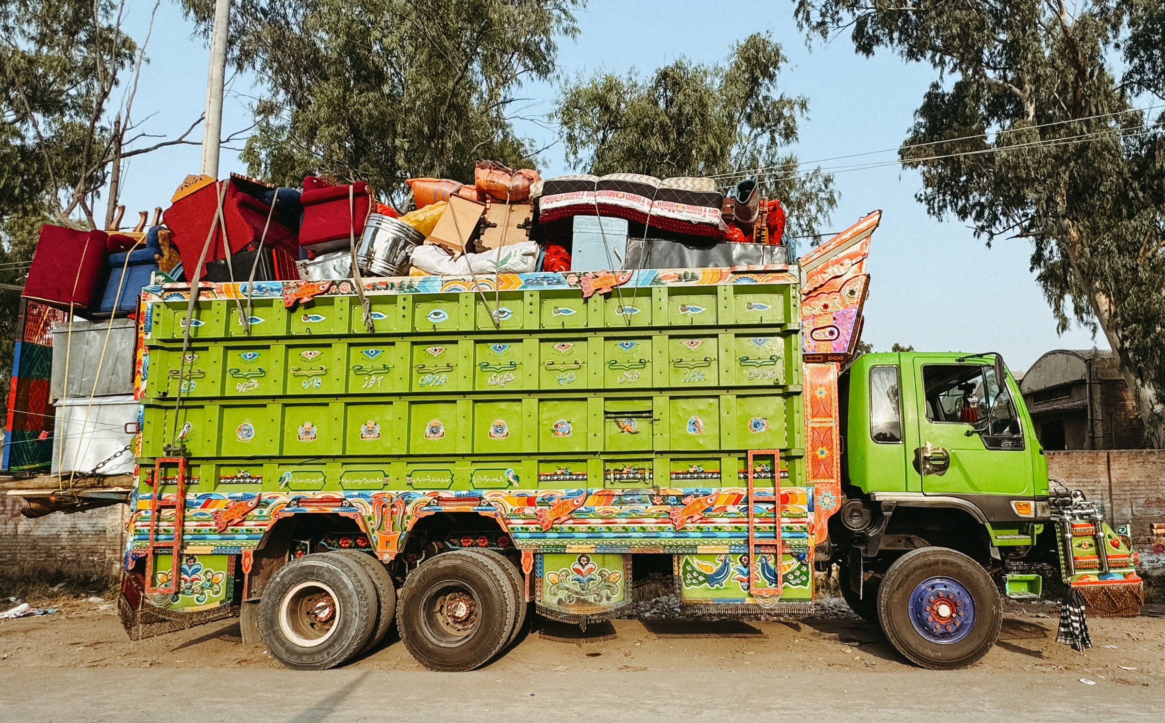 Camion vert décoré, chargé de marchandises et de textiles colorés.