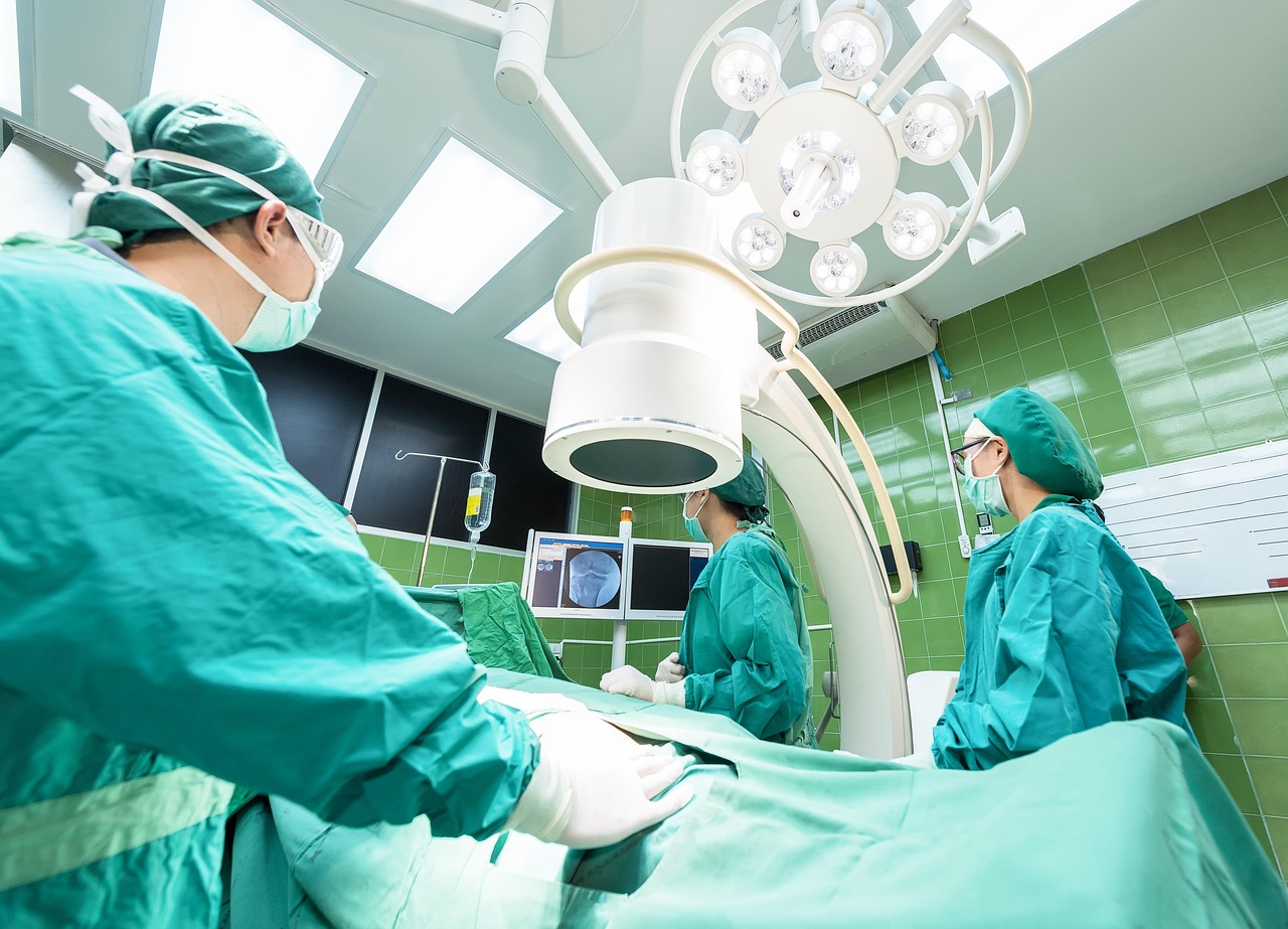 Surgeons in green scrubs perform an operation under bright lights in a modern operating room.