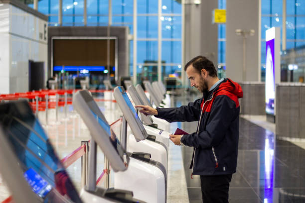 A man uses a self-service check-in kiosk at an airport while holding his passport.
