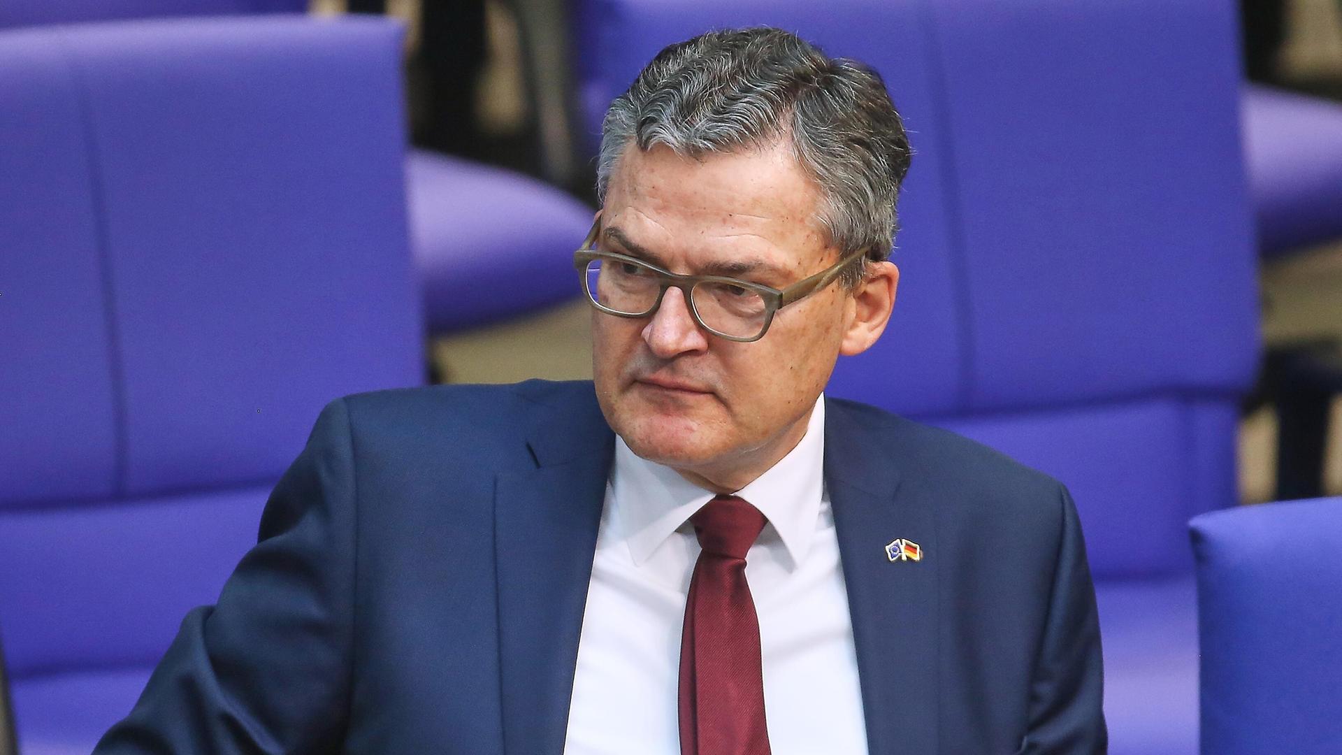 Der CDU-Abgeordnete Roderich Kiesewetter sitzt im Plenarsaal des Deutschen Bundestages. Er trägt eine Brille, einen blauen Anzug, weißes Hemd und rote Krawatte. 