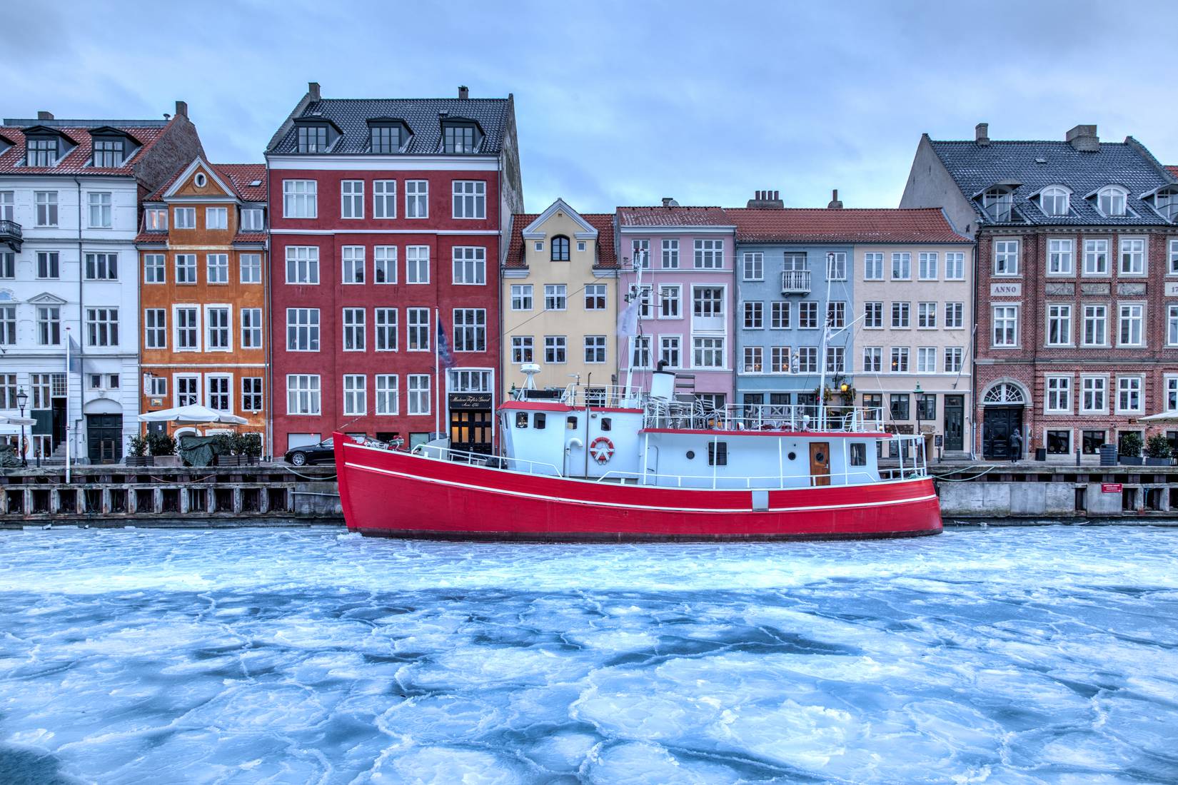 Nyhavn pier with colourful buildings and a red boat on the frozen canal, Copenhagen, Denmark