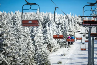 Skiers riding a chair lift via iStock / ViktorCap