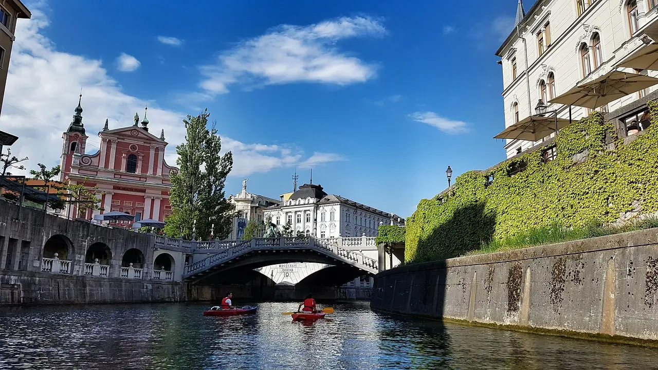 Kayakers paddle along the serene Ljubljanica River in Ljubljana, Slovenia, surrounded by eco-friendly attractions like lush greenery and historic architecture.