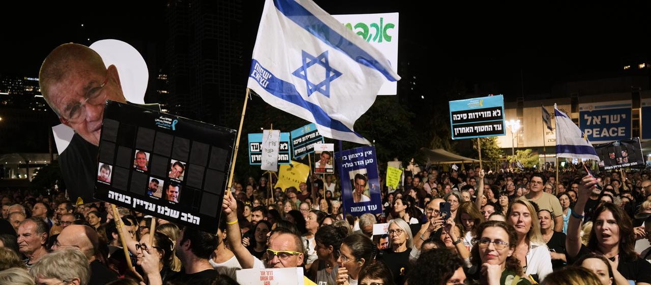 Menschen mit einer Israel-Fahne und Bannern protestieren in der Dunkelheit.