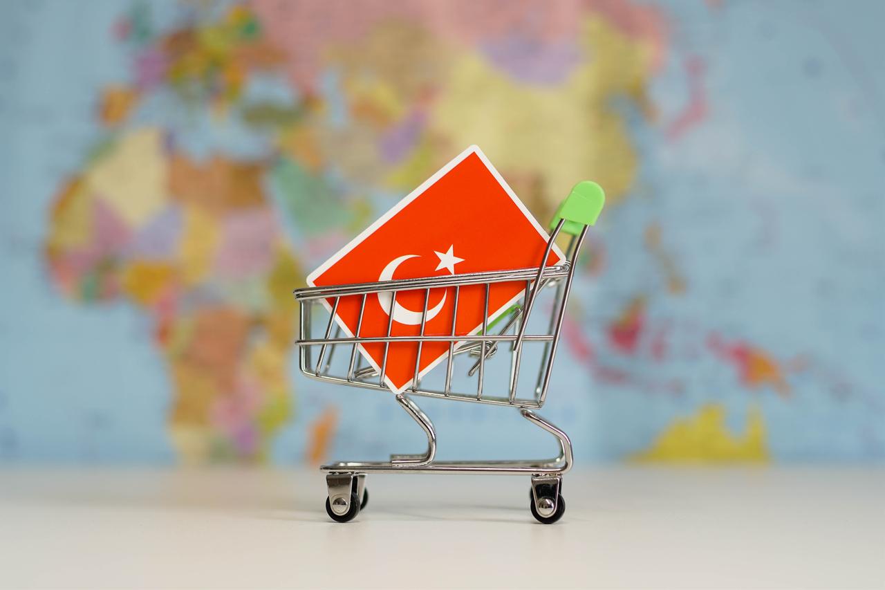 Turkish national flag in miniature shopping trolley cart, wit World map on the background, accessed on Nov. 20, 2025. (Adobe Stock Photo)