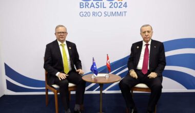Turkish President Recep Tayyip Erdogan and Prime Minister Anthony Albanese sit beside each other at a G20 meeting. A small table with the Australian and Turkish flags is between them.