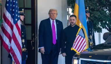 US President Donald Trump standing beside Ukrainian President Volodymyr Zelensky as he welcomes him to the White House. US and Ukrainian flags are beside them.