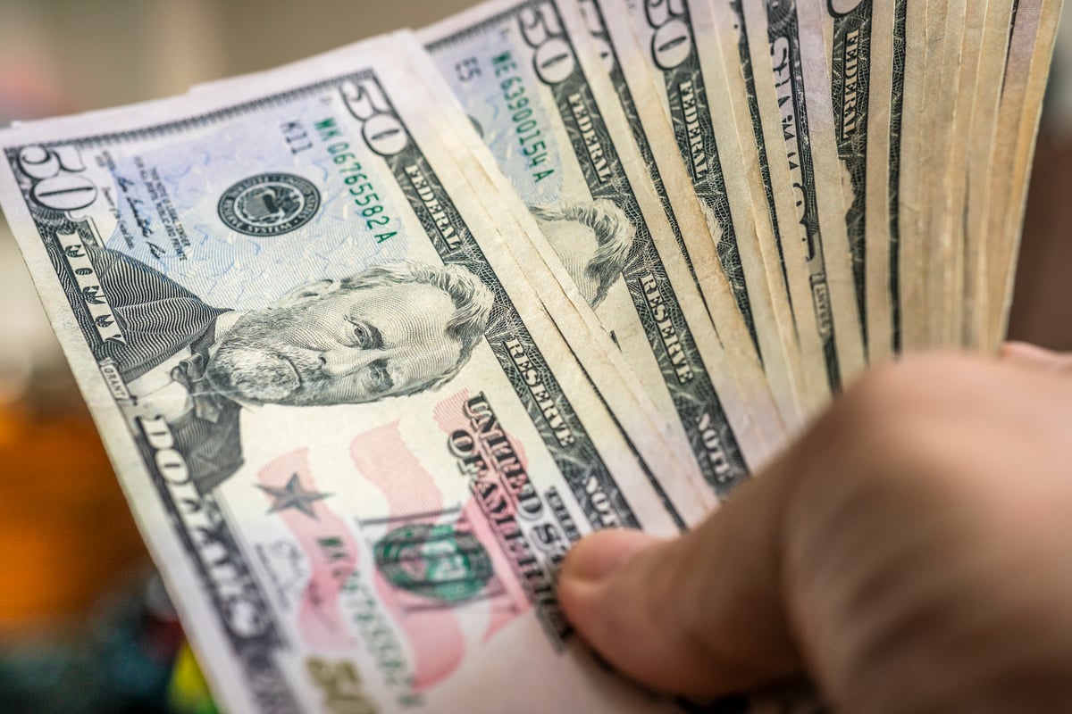 A hand holding a fan of fifty-dollar bills.