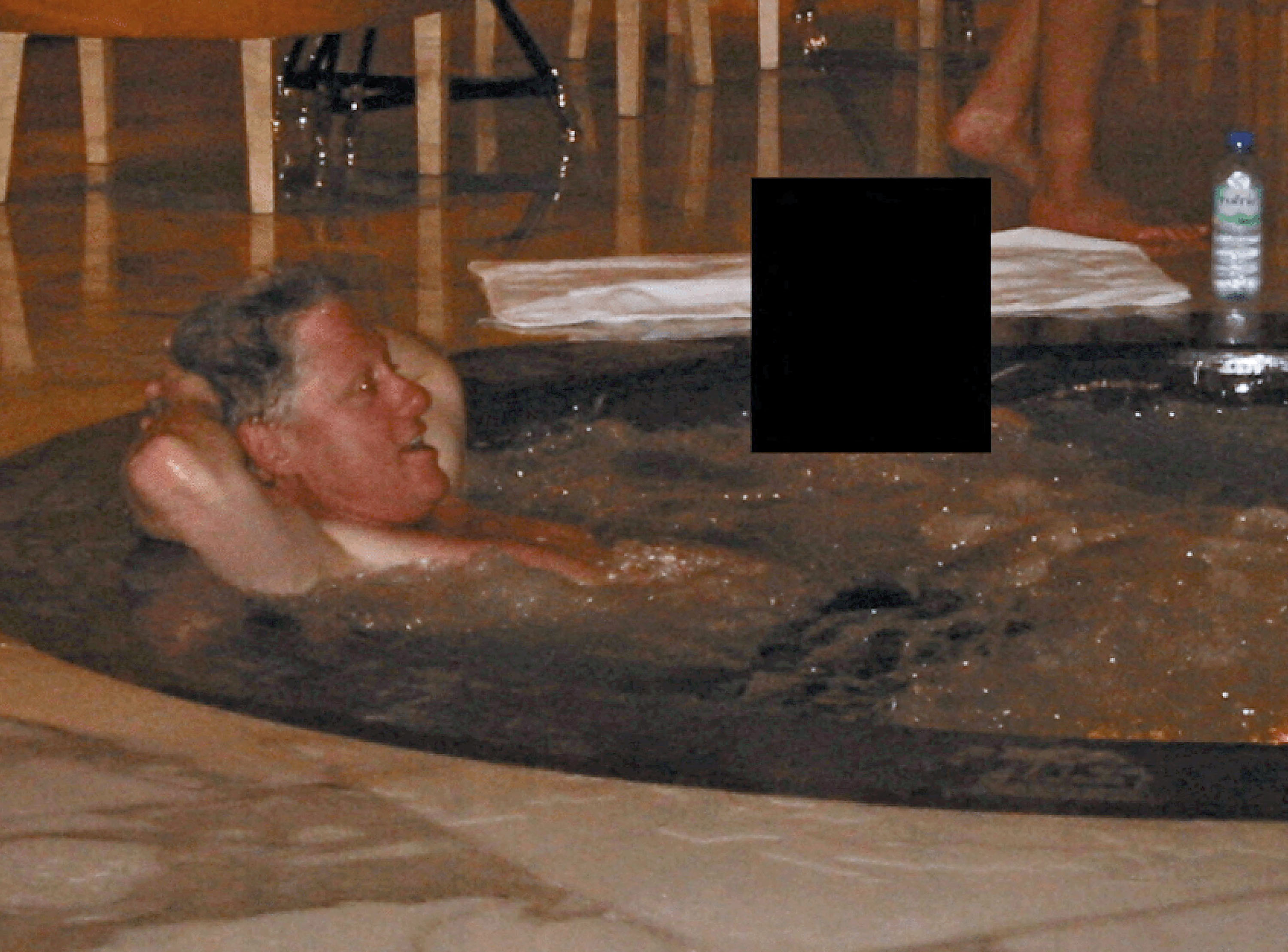 Former U.S. President Bill Clinton in a hot tub with his hands behind his head.