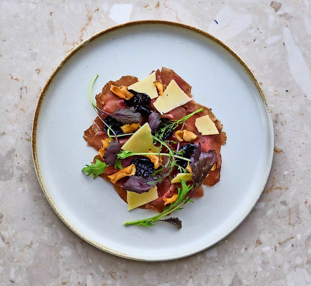 Carpaccio with cheese, mushrooms, and greens on a white plate.