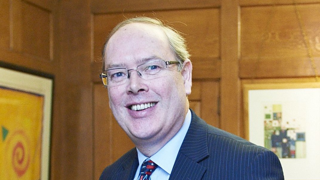 Andrew Sentance, member of the Monetary Policy Committee of the Bank of England, smiling and leaning on a desk.