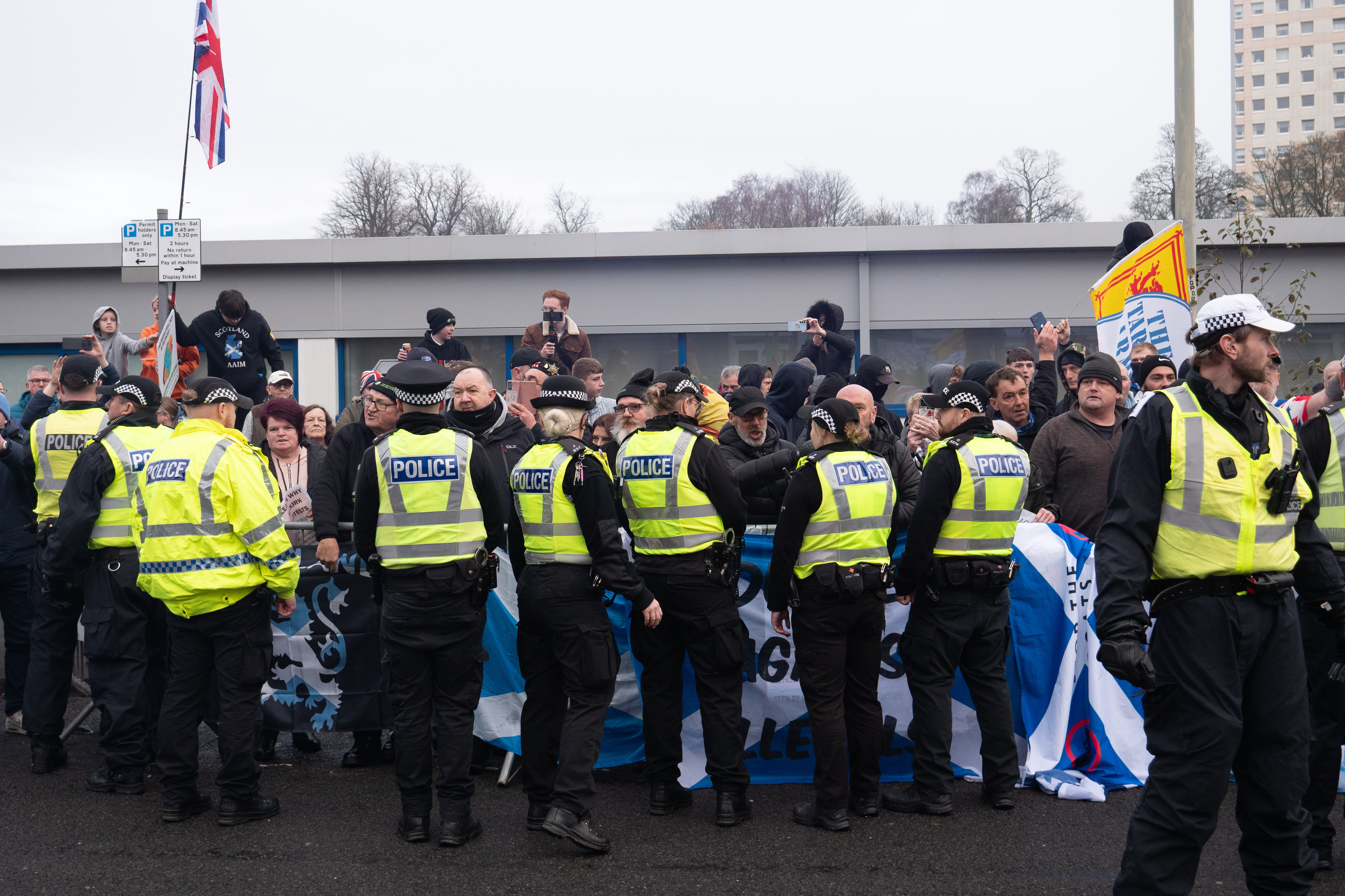Police officers wearing bright yellow vests standing in a crowd of protesters with flags and signs.