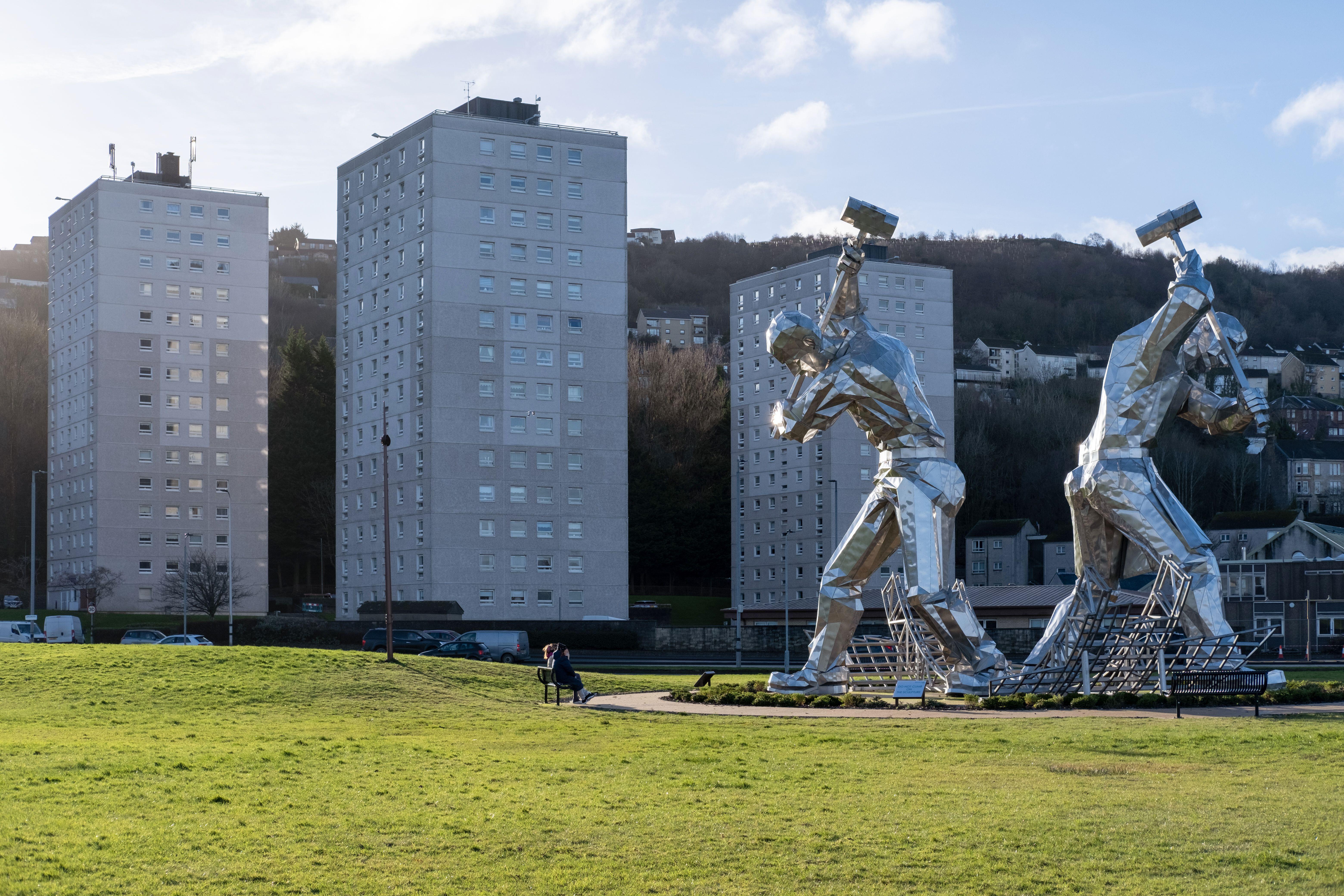 Two giant shipbuilders sculptures by John McKenna ("The Skelpies") in Port Glasgow, Scotland, with tower blocks in the background.