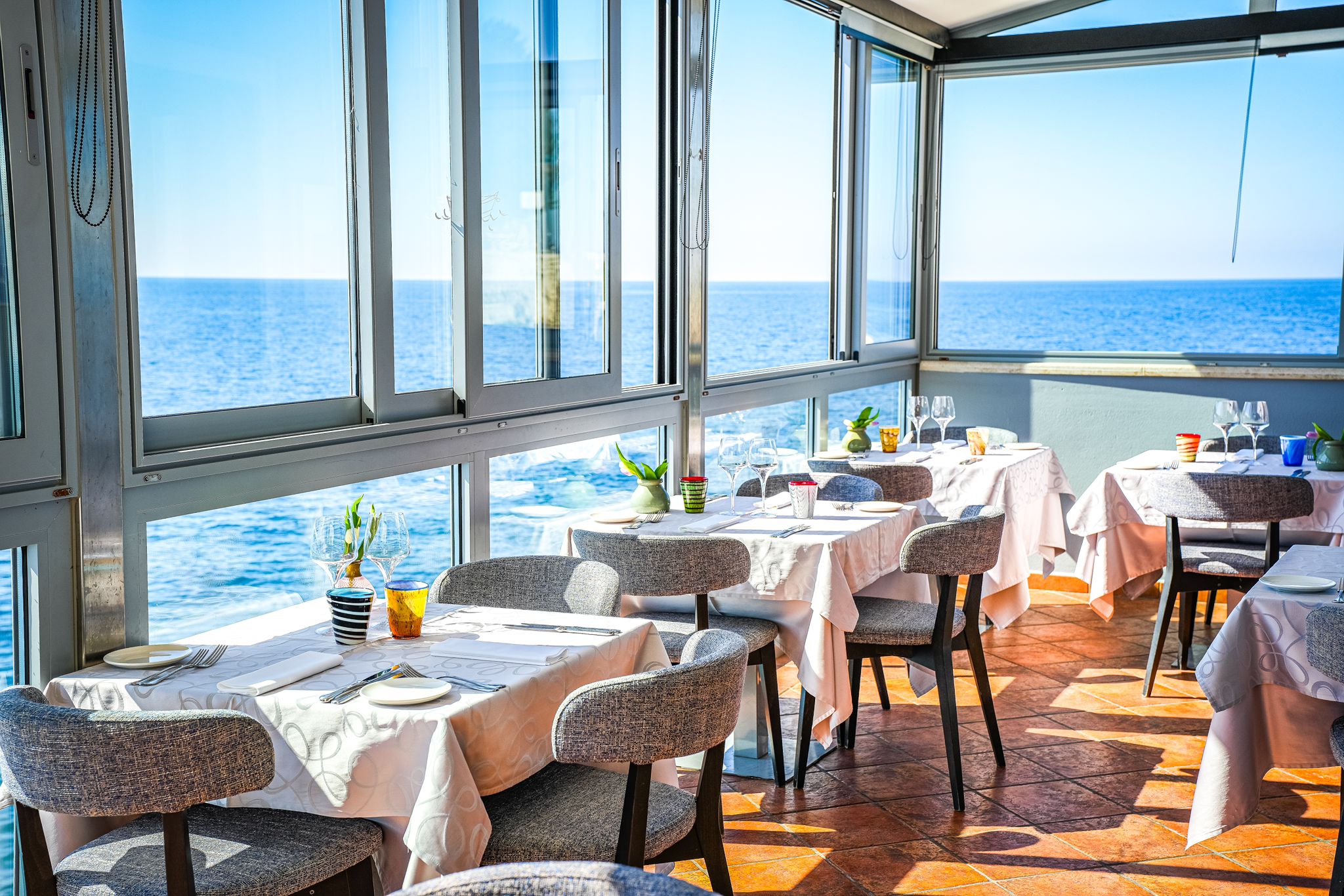 A restaurant dining room at Puntulina in Rovinj, Croatia, with tables set with white tablecloths and views of the blue sea.