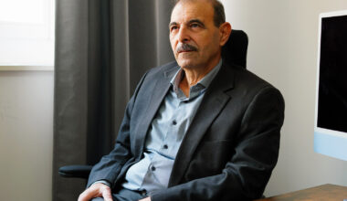 A man in a suit leans back in a chair at his desk, looking contemplatively into the distance. Behind him is a darkened computer monitor. He is Anwar al-Bunni, one of a million Syrian refugees who came to Germany to flee the Assad regime