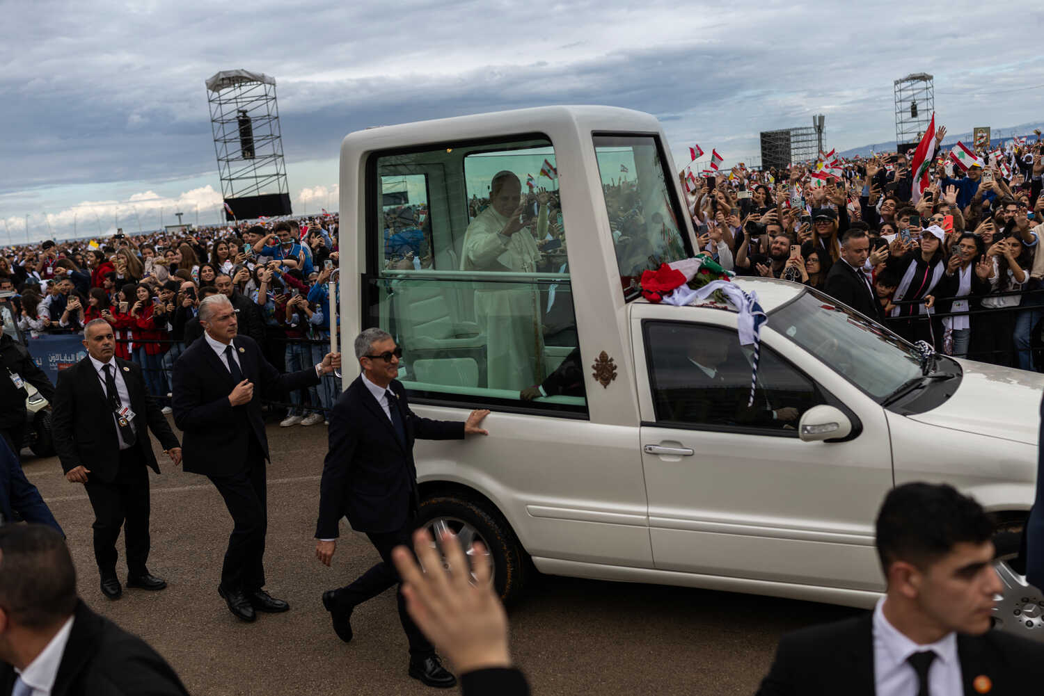 A white vehicle carries Pope Leo XIV past a large crowd waving flags.