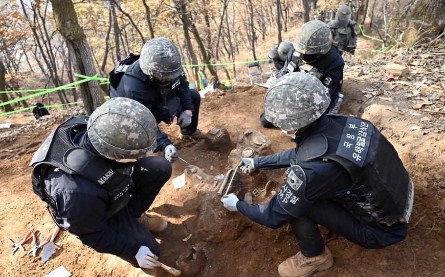 South Korean troops kneel down in the dirt to dig for remains.