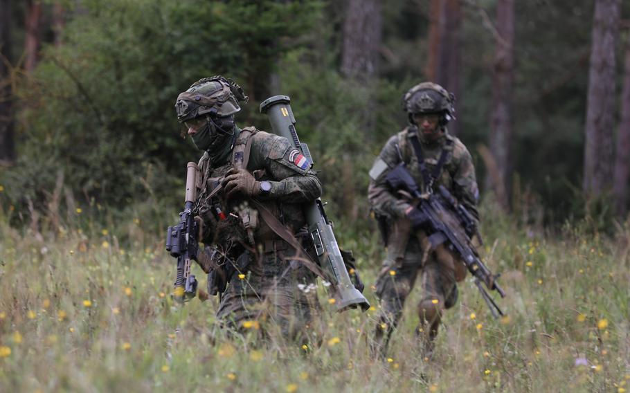 Two masked service members in a forest area.