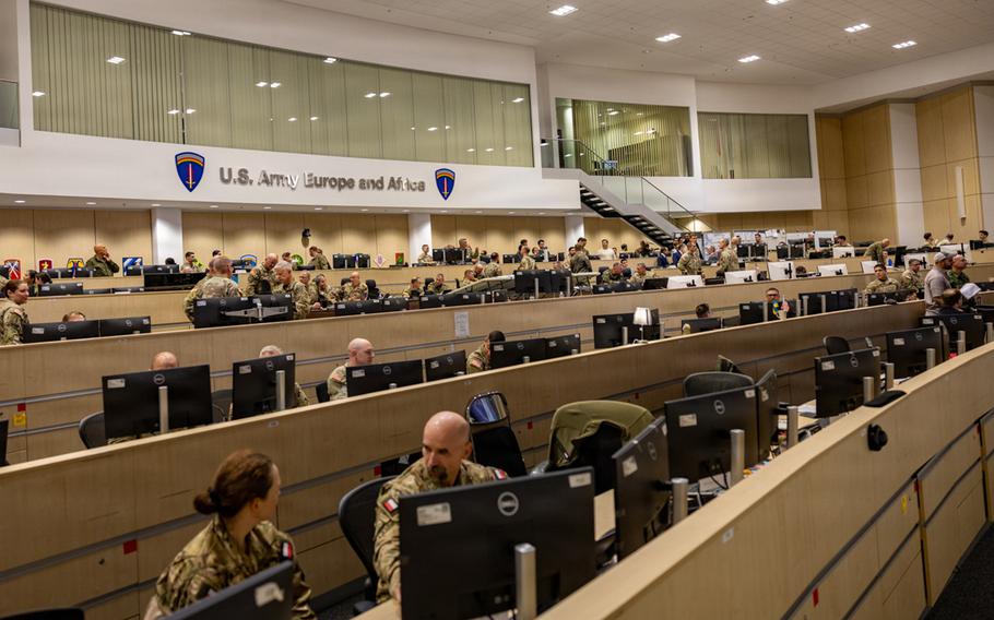An auditorium-like room with rows of computer monitors and uniformed service members.