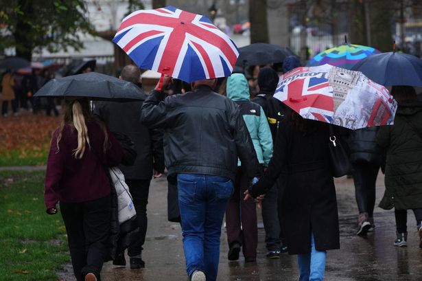 People shelter from the rain beneath Union Jack umbrellas in Green Park, central London