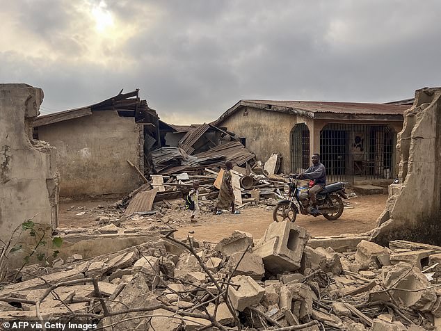 Residents and a motorcyclist move between destroyed structures in Offa on December 27, 2025 caused by debris from expended munitions that fell from US strikes on unspecified militants linked to the Islamic State group in Nigeria