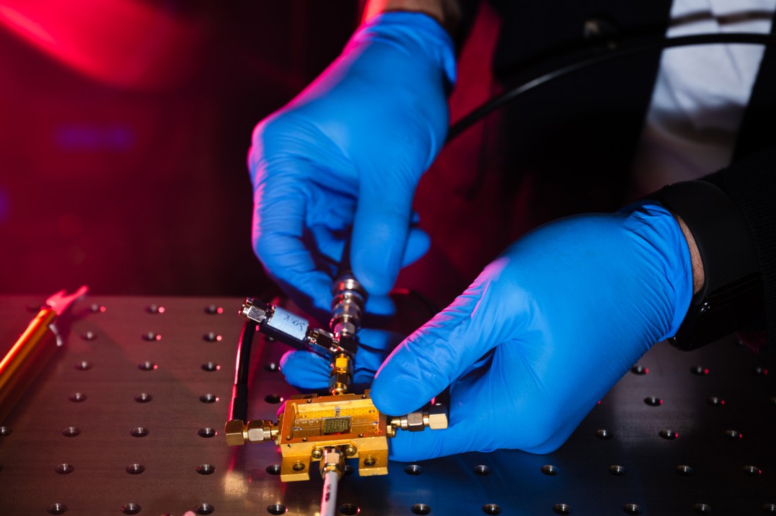 A pair of hands wearing blue latex gloves plugs a wire into the gold housing of a sensor.