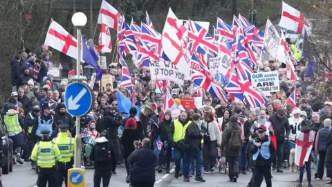Eddie Mitchell A large group of protesters marching on the street and holding Union Jack and St George flags.