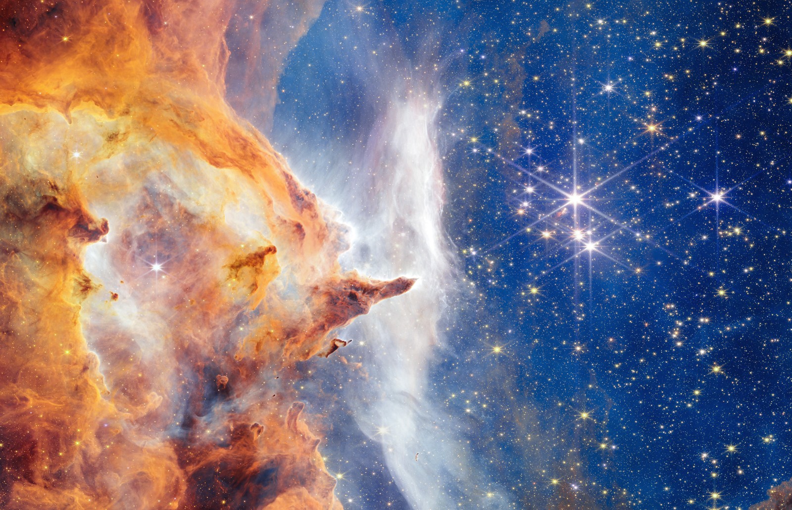 A dark and dense cloud of dust takes up the left half of the image, with a cluster of glittering white stars at right, all backdropped by many more-distant stars.