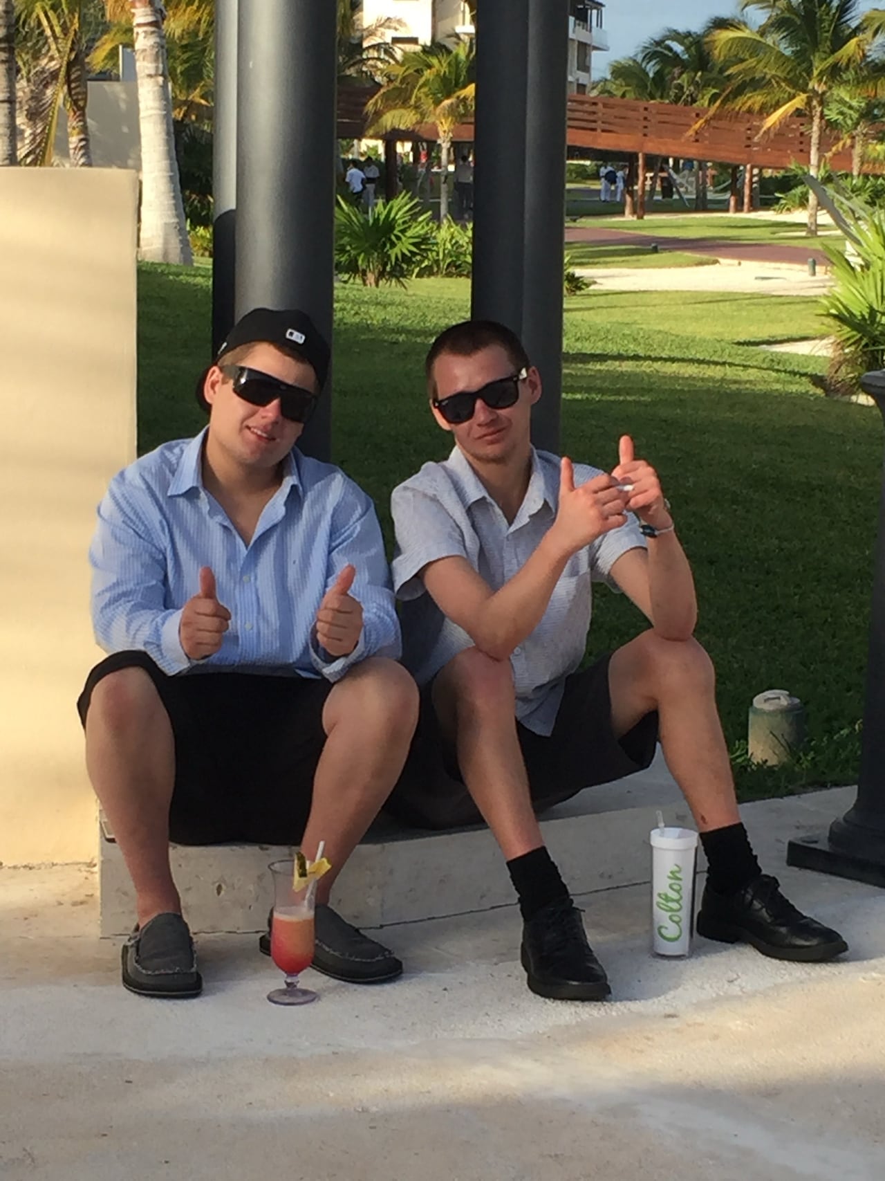 Two young men are shown posing for a photo, sitting on a cement block.