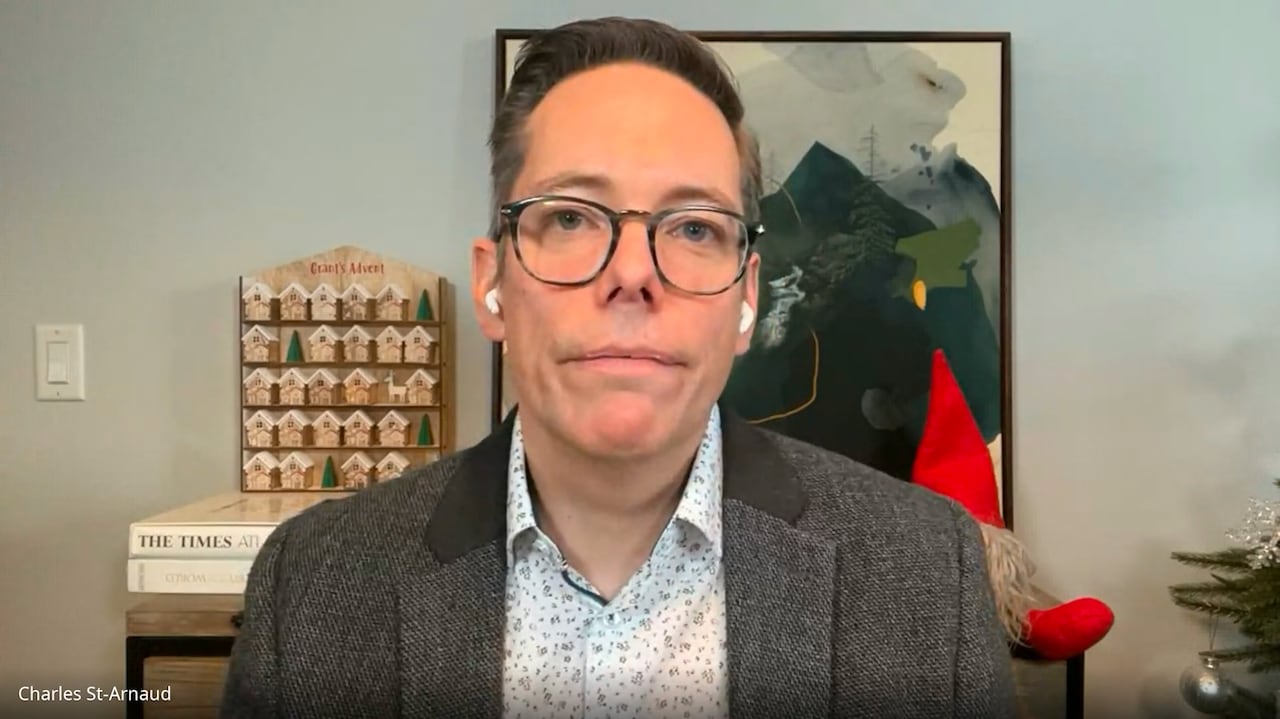 A man with glasses is seen in front of a painting.