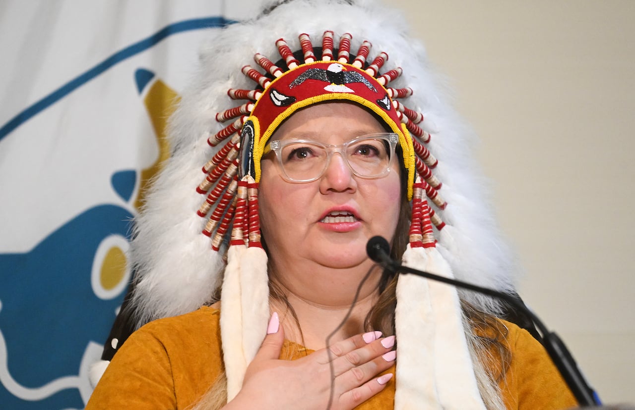 A woman wearing a headdress speaks at a microphone.
