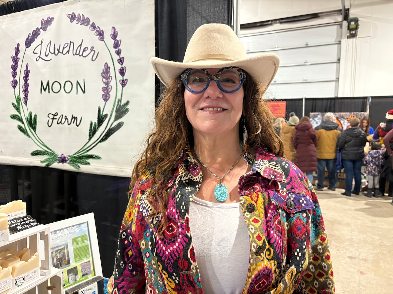 A white woman with curly golden brown hair, wearing glasses and a hat.