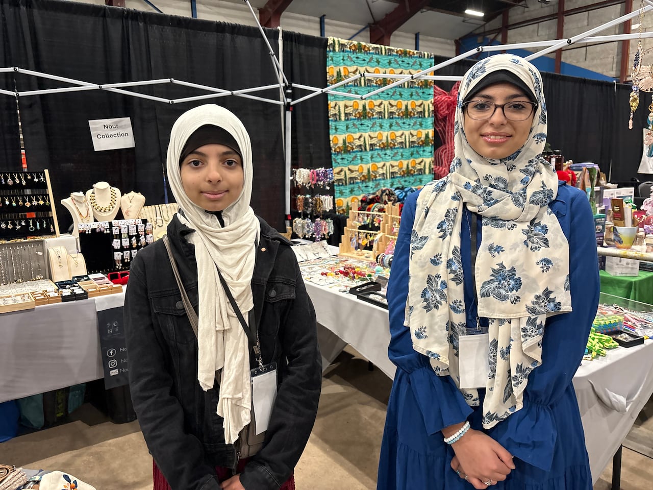 Two brown girls wearing hijabs. The one on the right is taller and she wears glasses.