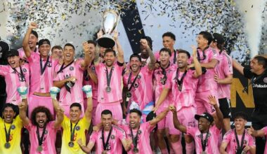 A soccer team in pink jerseys raises a trophy after winning a championship game.