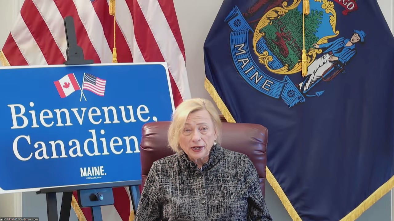 A woman sitting in a chair, speaking in front of a sign that says, 'Bienvenue Canadiens'
