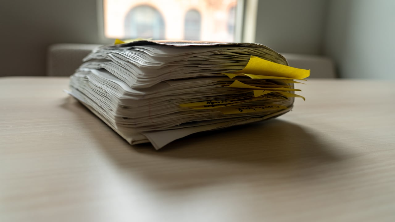 A dog-eared scrapbook sits on a wooden table overflowing with yellow sticky notes and other inserts.
