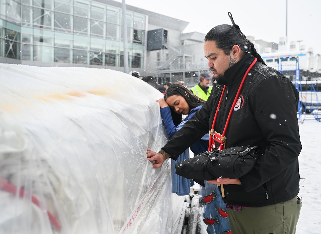 A woman leans her head on a piece of cargo while a man closes his eyes and touches it.