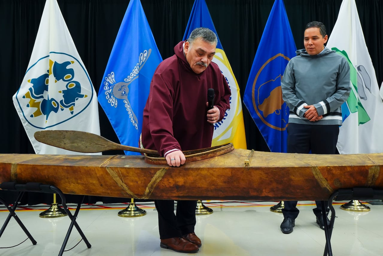 Two men stand next to an old kayak on display.
