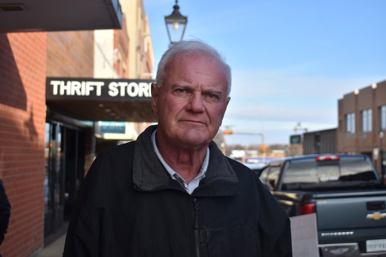A man with gray hair stands on a street. 