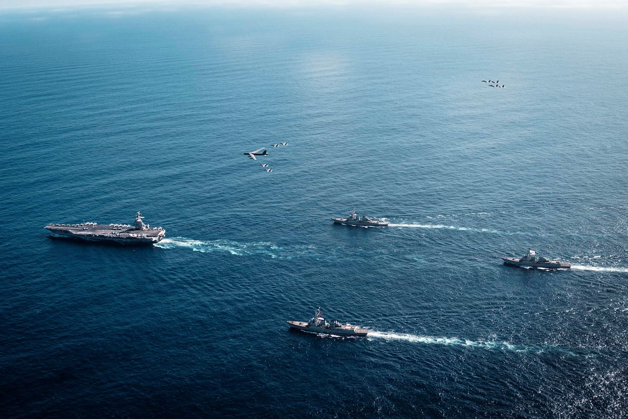 A bird's-eye view of a group of ships and a plane moving in the same direction, along the Caribbean Sea