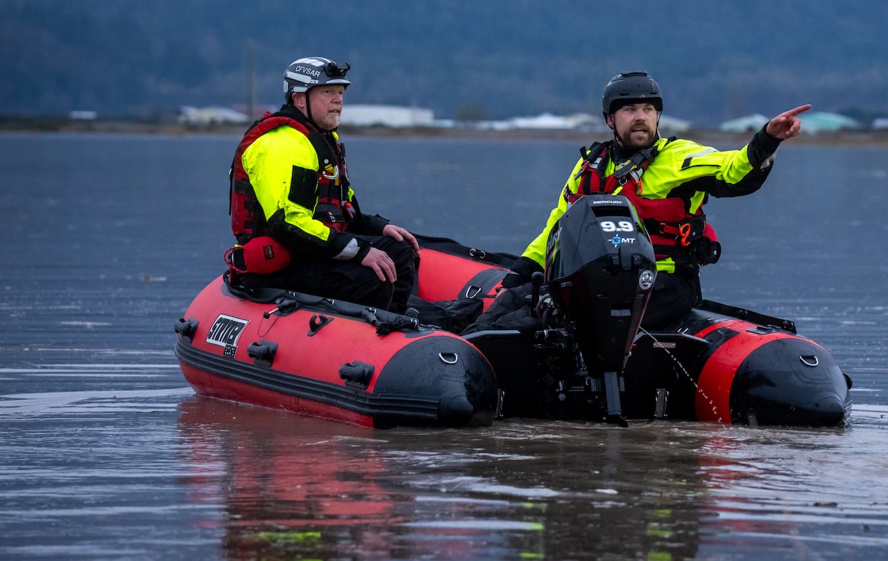 Two men wearing high-vis vests point on a boat.