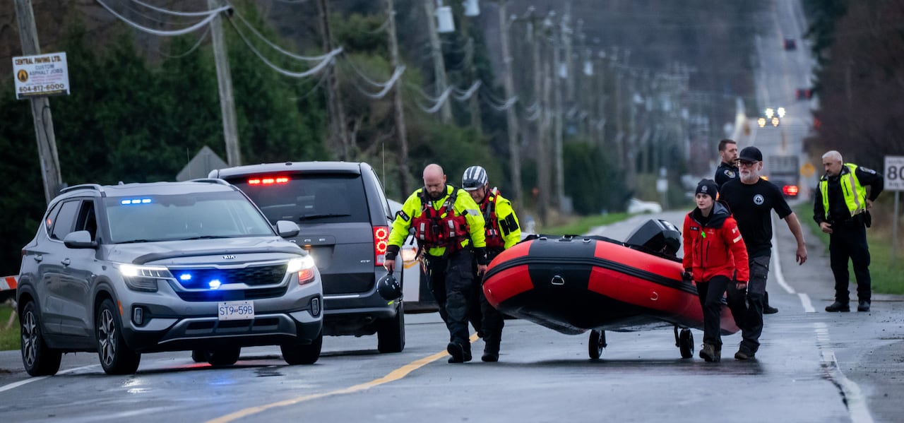 A number of people carry a raft through a street with emergency vehicles visible.