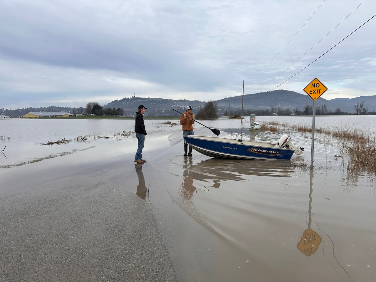 Two men get off a fishing boat as floodwaters inundate parts of a highway.