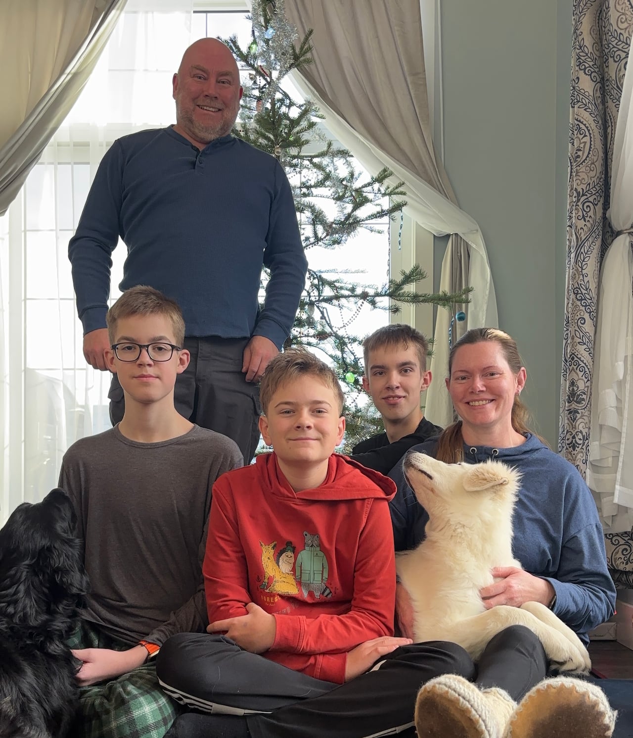 A family smiles in front of a Christmas tree. 