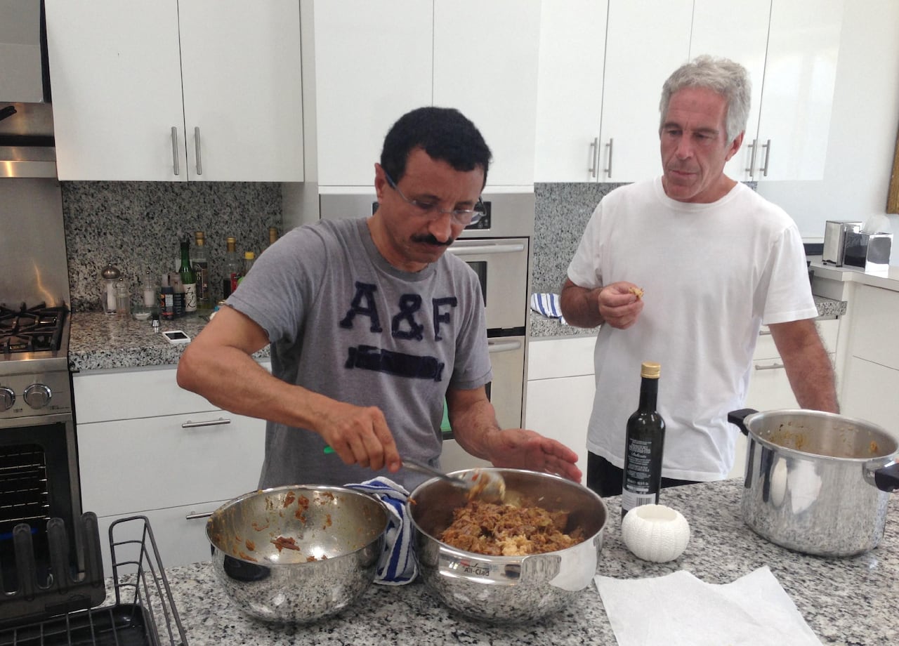 Sultan Ahmed bin Sulayem, with black hair and wearing glasses and a grey t-shirt with the letters A & F, standing in a kitchen and mixing food in a stainless steel bowl on a counter top next to Jeffrey Epstein, with grey hair and in a white t-shirt.