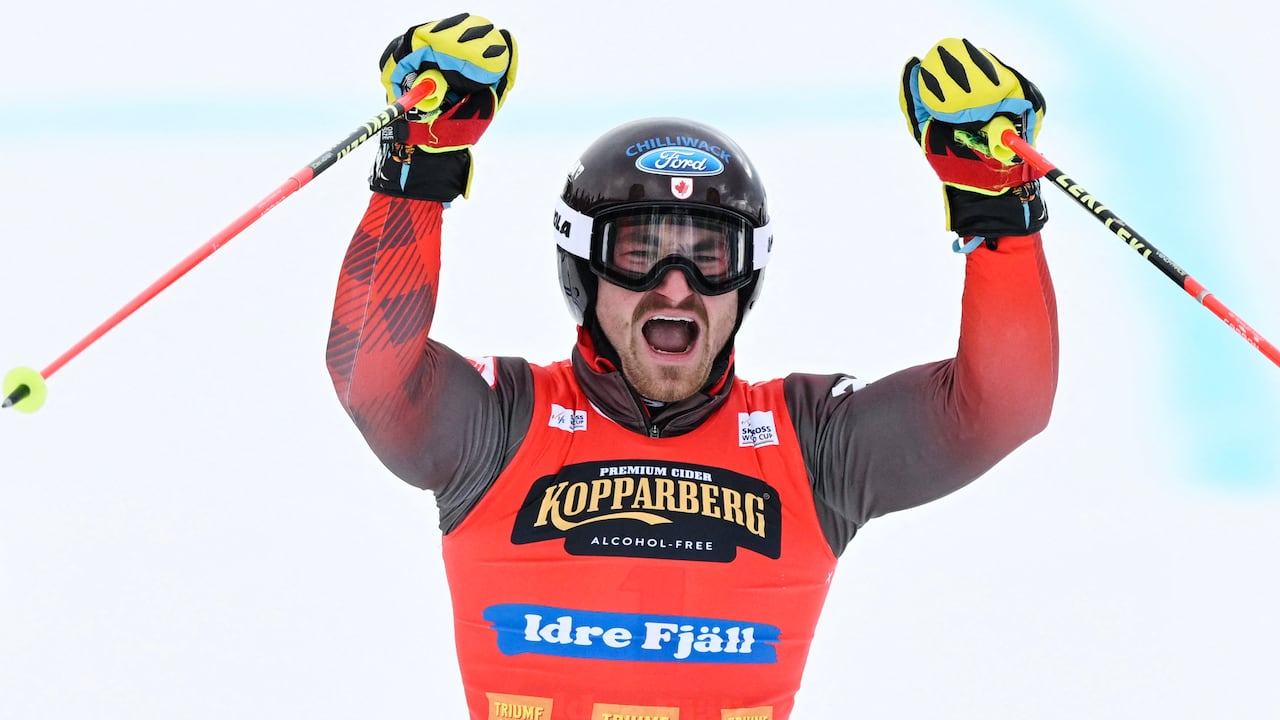 A men's skier raises his arms and ski poles over his head in celebration.