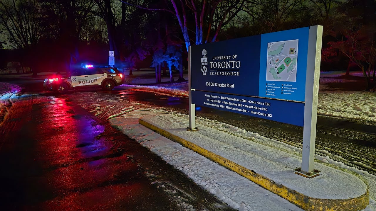 A Toronto police cruiser with its lights on parked in front of a University of Toronto Scarborough sign reading 130 Old Kingston Road